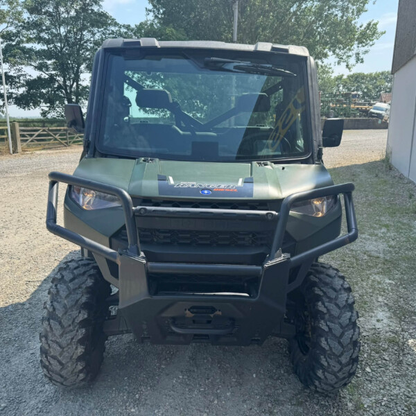 Front view of a green Polaris Ranger UTV with large tires and a protective bumper, parked on gravel outdoors.