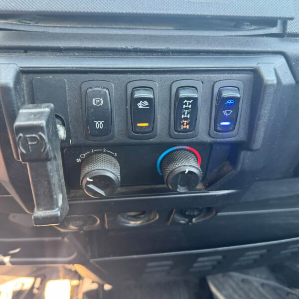 Dashboard panel with four vertical switches: electronic parking brake, a switch with an orange indicator, a differential/axle switch, and a windshield wiper/washer switch with a blue light; climate knobs below.