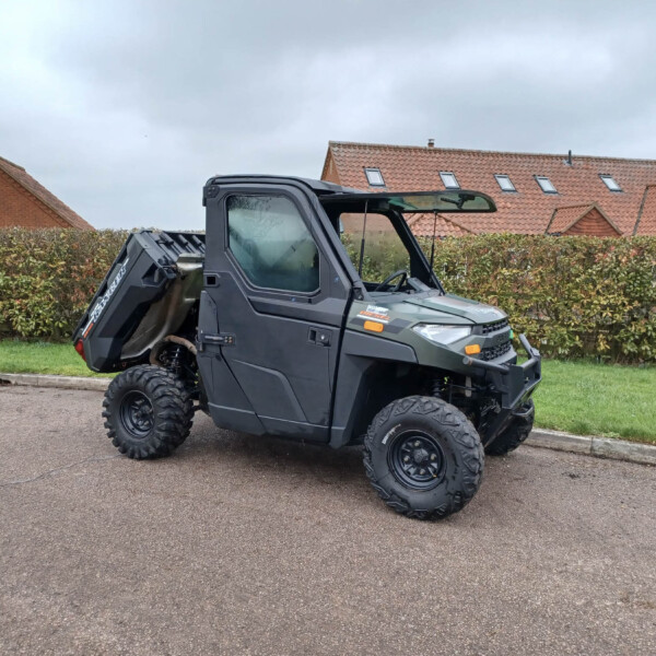 Rugged black off-road utility vehicle parked on a street, with hedges and red-tiled houses in the background.