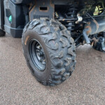 Close-up of a rugged off-road vehicle rear wheel and suspension showing muddy tires, rust, and exposed exhaust components