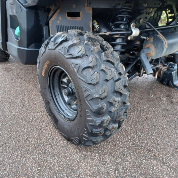Close-up of a rugged off-road vehicle rear wheel and suspension showing muddy tires, rust, and exposed exhaust components
