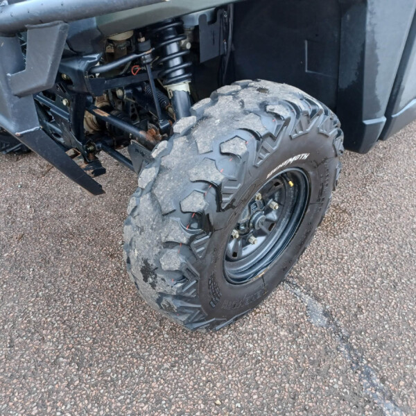 Close-up of a rugged off-road tire and exposed suspension on a dark vehicle, resting on gravel ground