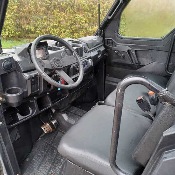 Rugged off-road vehicle interior with steering wheel, dashboard, and dirt-streaked black panels visible through an open door.