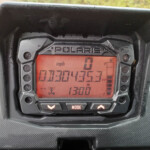 Polaris instrument cluster with a red backlit digital display showing speed in mph and status indicators inside a protective housing.