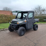 Gray off-road utility vehicle (UTV) parked on a residential driveway, with hedges and a red-tiled roof house in the background.