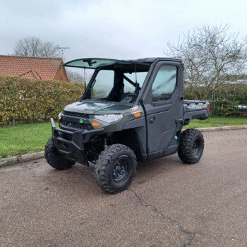 Gray off-road utility vehicle (UTV) parked on a residential driveway, with hedges and a red-tiled roof house in the background.