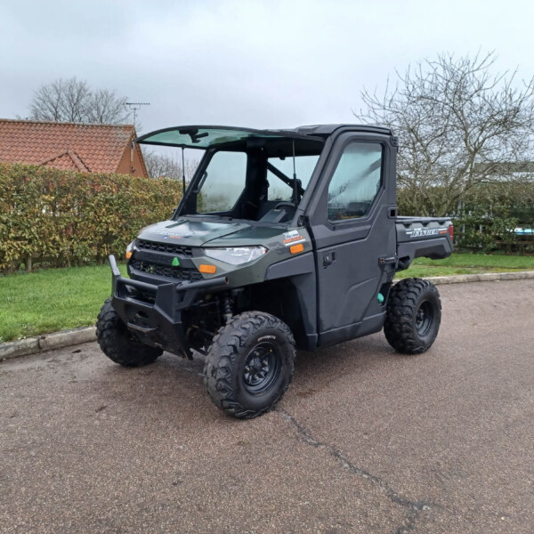 Gray off-road utility vehicle (UTV) parked on a residential driveway, with hedges and a red-tiled roof house in the background.