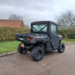 Black Polaris Ranger UTV parked on a suburban driveway with hedges and bare trees in the background under a cloudy sky