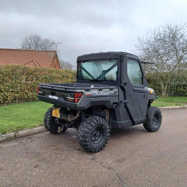 Black Polaris Ranger UTV parked on a suburban driveway with hedges and bare trees in the background under a cloudy sky