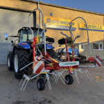 Blue New Holland tractor with multiple attached farming implements on a display yard in front of a brick building with New Holland Agriculture and Russell's signage.