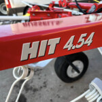Close-up of a red metal panel with large white numbers, with blurred equipment and wheels in the background.