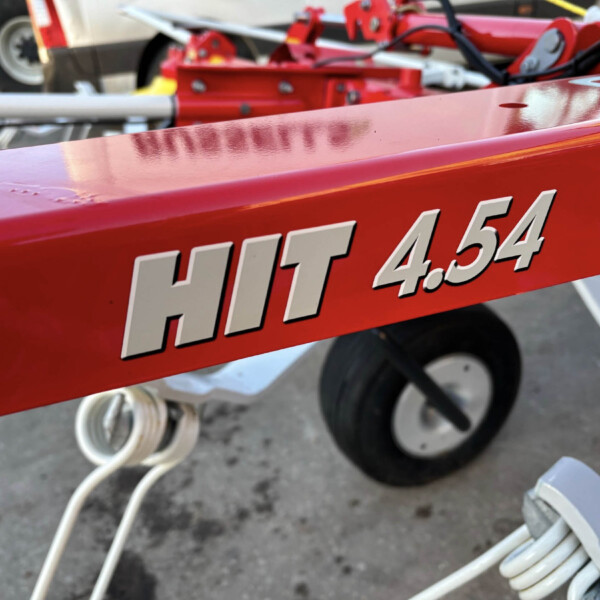 Close-up of a red metal panel with large white numbers, with blurred equipment and wheels in the background.
