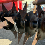 Close-up of rusted metal blades on a red agricultural implement, overlapping sharp triangular edges outdoors
