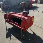 Red agricultural tiller attachment labeled 'Spiker 1350' in a yard with parked tractors and pallets in the background.