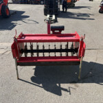 Front view of a red agricultural cultivator with rotating discs in a parking lot, forklift in background.
