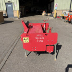 Red Spiker 1350 garden/rail maintenance machine in foreground with safety labels, parked on asphalt outside a workshop.