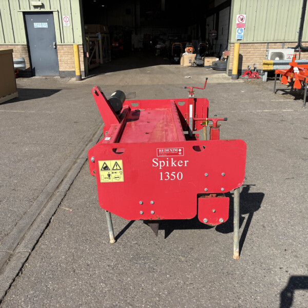 Red Spiker 1350 garden/rail maintenance machine in foreground with safety labels, parked on asphalt outside a workshop.