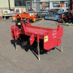 Red agricultural implement labeled 'Spiker 1350' with multiple tines, parked in a yard near a blue metal trailer and industrial equipment.