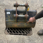 Rusty industrial equipment mounted on a blue-green metal frame, with a worker's boot visible on the right near a storm drain grate.