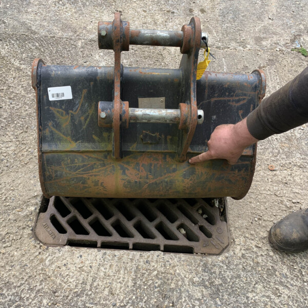 Rusty industrial equipment mounted on a blue-green metal frame, with a worker's boot visible on the right near a storm drain grate.