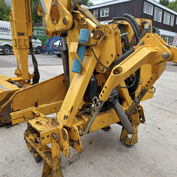 Close-up of yellow construction machinery ( excavator arms and hydraulic cylinders ) in a yard with vans in the background, showing weathered paint and grime for an equipment display.
