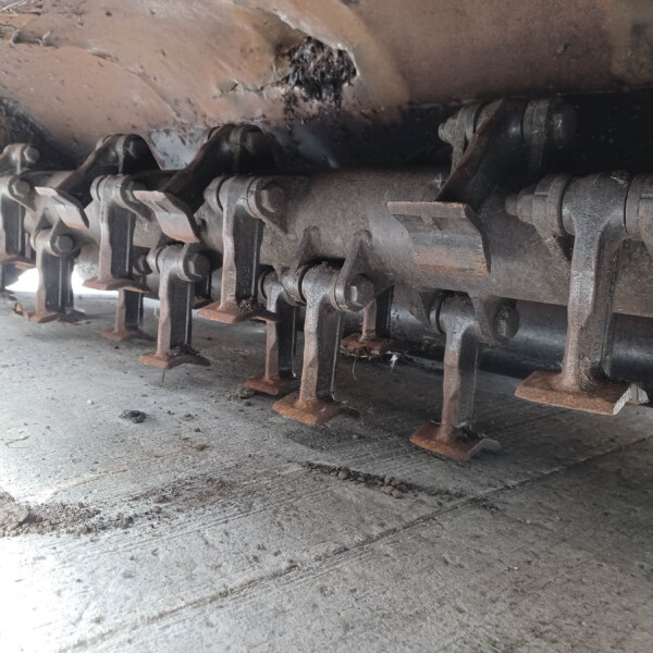 Close-up of a rusty undercarriage with track links and rollers from heavy machinery, showing dust and corrosion