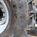 Close-up of a large off-road tractor tire with deep tread blocks and a silver rim visible on the left.