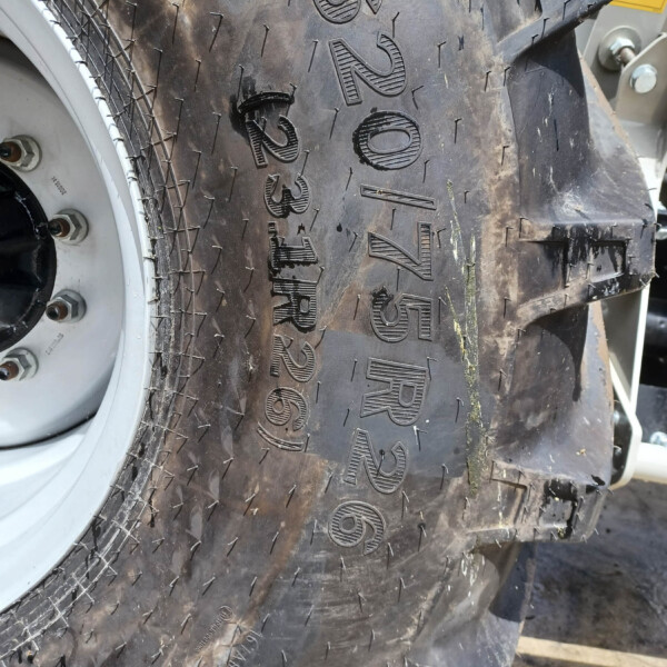 Close-up of a large off-road tractor tire with deep tread blocks and a silver rim visible on the left.