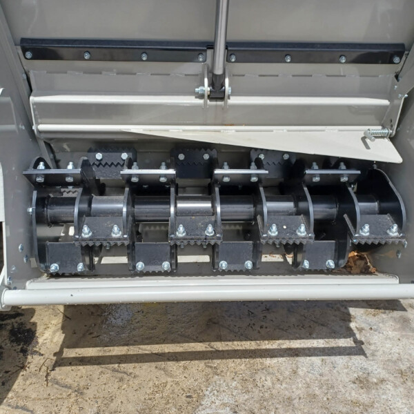 Close-up of an industrial machine showing metal rails, bolts, and a toothed roller assembly with black gear-like components and a white guard bar below.