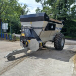 Mobile industrial shredder/chipper mounted on a trailer with a large hopper and conveyor, parked in a driveway with trees in the background.