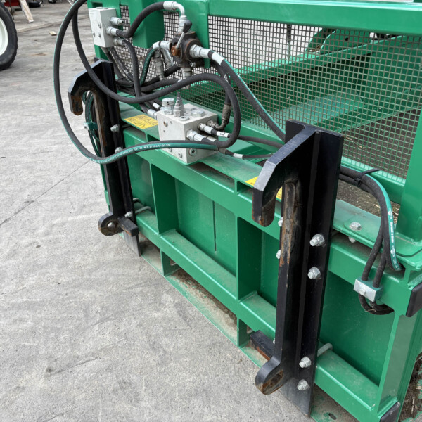 Close-up of a green industrial hydraulic machine with hoses, metal fittings, and a mesh guard behind it.