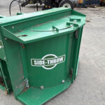 Green Side-Throw industrial waste hopper in a yard, with soil and debris and a UK flag sticker on the side.