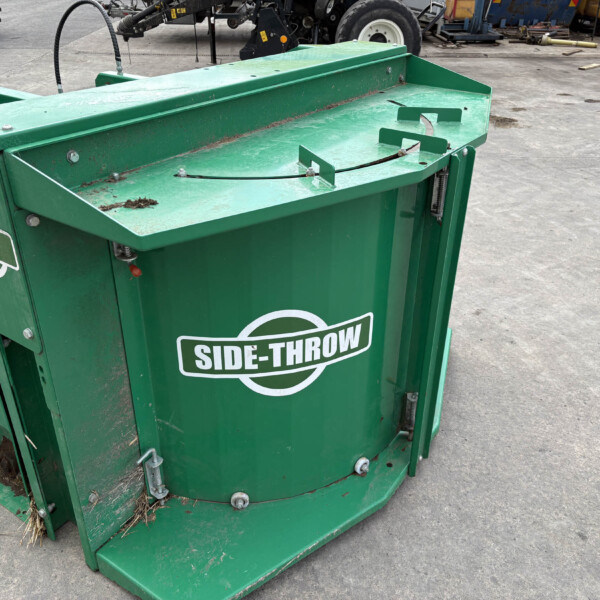 Green Side-Throw industrial waste hopper in a yard, with soil and debris and a UK flag sticker on the side.