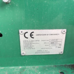 Close-up of a silver certificate plate bolted to a green industrial surface; reads 'CERTIFICATE OF CONFORMITY' and includes product details and serial information.