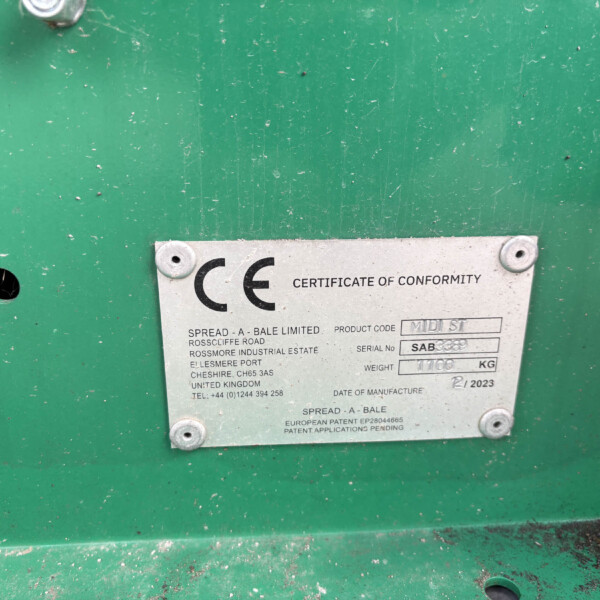 Close-up of a silver certificate plate bolted to a green industrial surface; reads 'CERTIFICATE OF CONFORMITY' and includes product details and serial information.