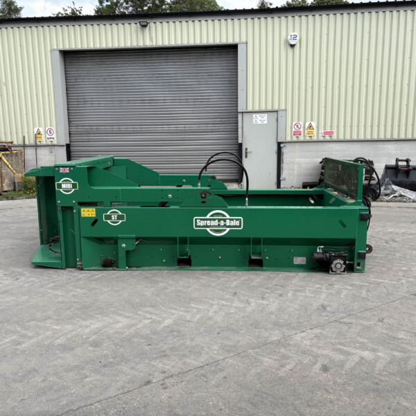 Green Spread-a-Bale bale wrapper in front of a beige corrugated metal warehouse with a large roll-up door