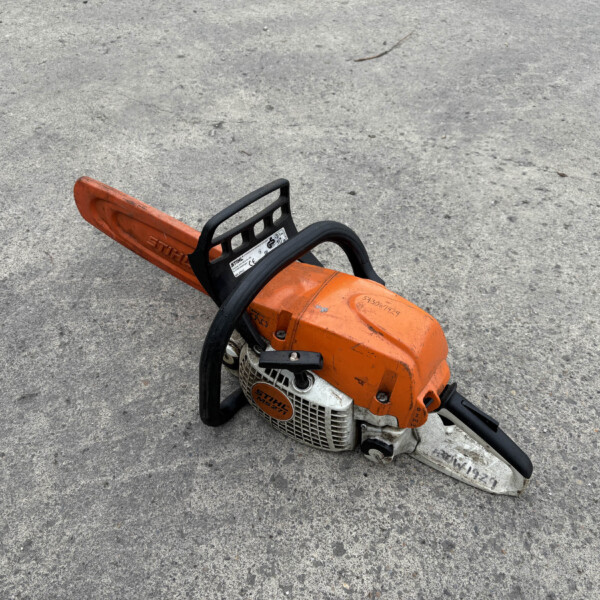 Orange Stihl chainsaw resting on a rough grey concrete surface with a black handle visible