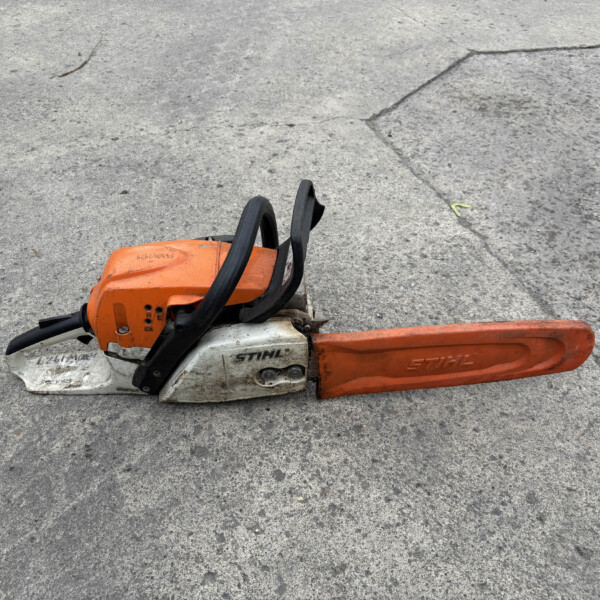 Orange STIHL chainsaw resting on rough concrete pavement with a black handle visible.