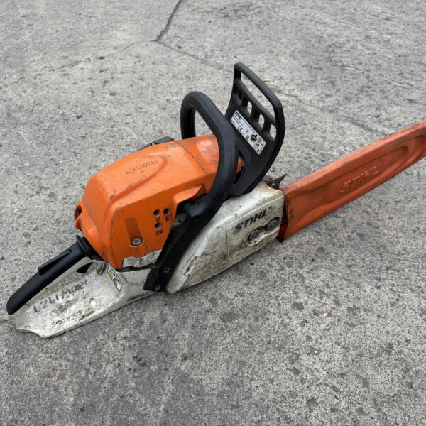 Orange and white gas-powered chainsaw resting on a gray concrete surface, with the bar extending to the right.