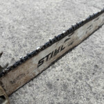 Close-up of a rusty, dirty chainsaw bar and chain on a rough concrete surface.