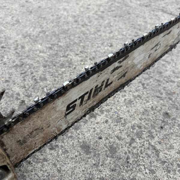 Close-up of a rusty, dirty chainsaw bar and chain on a rough concrete surface.