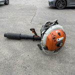 Cut-off saw with an orange body lying on a paved surface, with parked cars in the background.