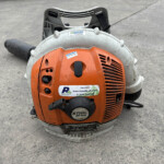 Close-up of an orange STIHL BR 500 leaf blower on a concrete surface, showing its front vent, controls, and worn exterior stickers.