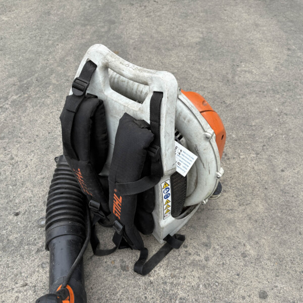 Portable concrete-cutting saw with orange engine housing and black safety straps resting on a gray pavement surface, hose attached to the tool.