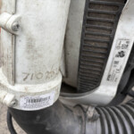 Close-up of a dusty white plastic backpack blower component with a barcode label and worn surface.