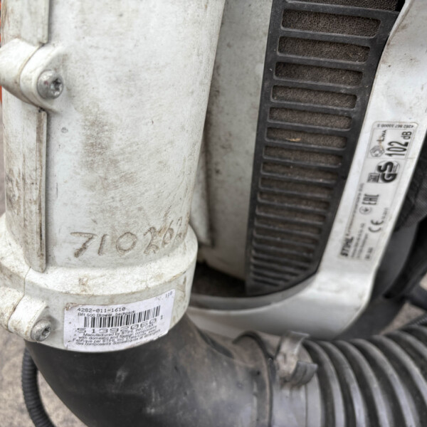 Close-up of a dusty white plastic backpack blower component with a barcode label and worn surface.
