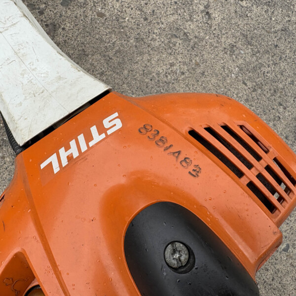 Close-up of an orange Stihl cut-off saw resting on a rough concrete surface, showing the blade guard and vents.