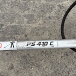 White cylindrical pipe with safety labels lying on rough concrete, a black coiled cable runs nearby.