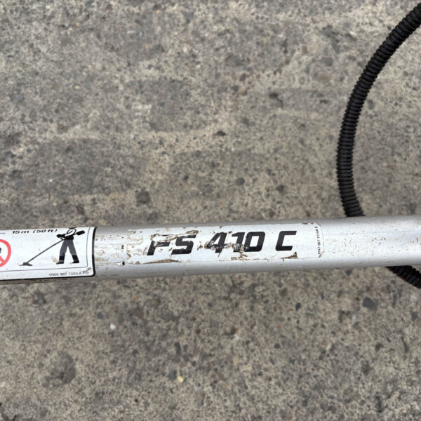 White cylindrical pipe with safety labels lying on rough concrete, a black coiled cable runs nearby.