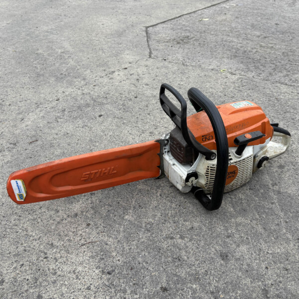 Orange STIHL chainsaw lying on a rough concrete surface, bar and handles visible.